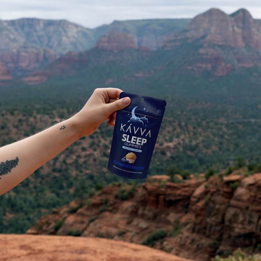 tattooed-womans-hand-holding-blueberry-muffin-sleep-kavva-delta-9-gummy-packaging-on-red-rock-with-red-rock-mountains-in-background-kavva-2023